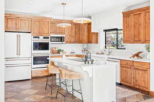 Kitchen with white appliances, a breakfast bar, brown cabinetry, decorative light fixtures, and recessed lighting