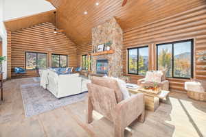 Living room with high vaulted ceiling, a stone fireplace, ceiling fan, hardwood / wood-style floors, and rustic walls