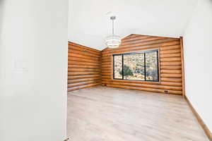 Unfurnished room featuring rustic walls, light wood finished floors, vaulted ceiling, and a chandelier