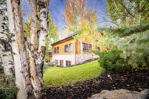 View of property exterior featuring a chimney, a lawn, stone siding, and log exterior