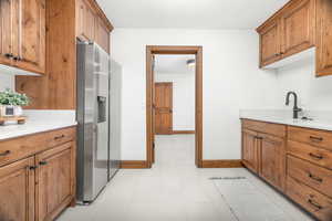 Kitchen with brown cabinets, stainless steel refrigerator with ice dispenser, light tile patterned floors, and light stone counters