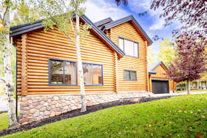 View of property exterior with log siding, a lawn, and a garage