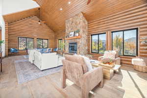 Living area featuring high vaulted ceiling, a fireplace, a ceiling fan, hardwood / wood-style flooring, and rustic walls