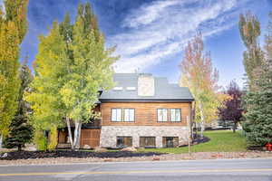 View of property exterior featuring stone siding, log siding, a chimney, a wooden deck, and a shingled roof
