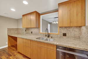Kitchen with wood finished floors, light stone countertops, dishwasher, backsplash, and recessed lighting