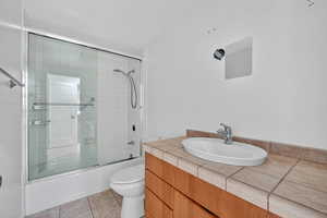 Full bathroom with bath / shower combo with glass door, vanity, and light tile patterned floors