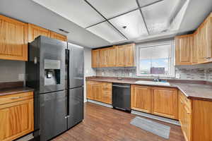 Kitchen with stainless steel fridge with ice dispenser, dark wood-style floors, dishwasher, decorative backsplash, and dark countertops