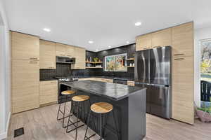 Kitchen with light brown cabinetry, stainless steel appliances, a breakfast bar, open shelves, and recessed lighting