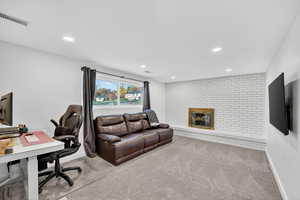 Carpeted home office featuring brick wall, recessed lighting, and a brick fireplace
