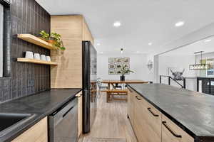 Kitchen featuring light brown cabinetry, dishwasher, light wood finished floors, recessed lighting, and freestanding refrigerator