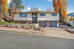 Split foyer home featuring brick siding, driveway, a chimney, and an attached garage