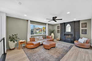 Living room featuring a brick fireplace, light wood finished floors, a ceiling fan, and recessed lighting