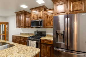 Kitchen featuring appliances with stainless steel finishes, light stone counters, and brown cabinets