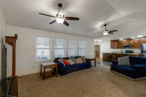 Living room with healthy amount of natural light, lofted ceiling, light carpet, and ceiling fan
