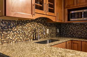 Kitchen with glass insert cabinets, brown cabinets, stainless steel microwave, light stone counters, and tasteful backsplash