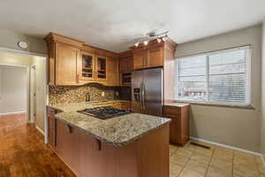 Kitchen with brown cabinets, a peninsula, glass insert cabinets, appliances with stainless steel finishes, and a breakfast bar area