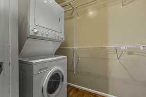 Washroom with dark wood-style floors and stacked washer / dryer