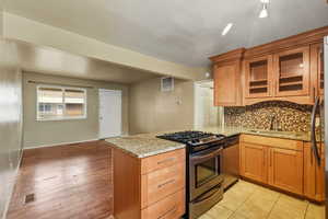 Kitchen with glass insert cabinets, appliances with stainless steel finishes, light stone counters, and a peninsula
