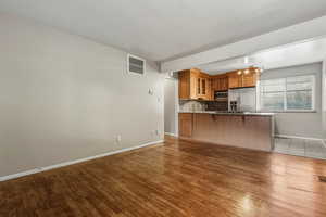 Kitchen with brown cabinets, a breakfast bar area, glass insert cabinets, dark wood-style floors, and appliances with stainless steel finishes