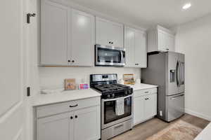 Kitchen featuring stainless steel appliances, light wood-type flooring, white cabinetry, recessed lighting, and light stone countertops