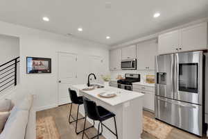 Kitchen featuring appliances with stainless steel finishes, light wood-style flooring, recessed lighting, a kitchen island with sink, and a breakfast bar area