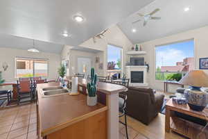 Kitchen with lofted ceiling, a center island with sink, hanging light fixtures, a kitchen bar, and a glass covered fireplace