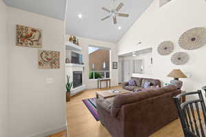 Living area featuring high vaulted ceiling, a ceiling fan, a glass covered fireplace, light wood-style floors, and recessed lighting