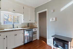 Kitchen with white cabinets, dishwasher, dark wood-style flooring, black microwave, and backsplash