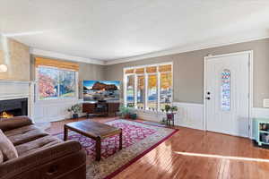 Living room featuring hardwood / wood-style flooring, a wainscoted wall, a decorative wall, a lit fireplace, and a textured ceiling