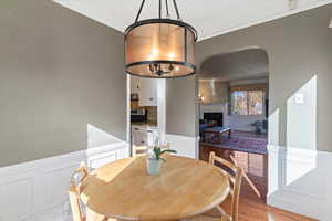 Dining space with a decorative wall, wainscoting, ornamental molding, light wood finished floors, and a chandelier