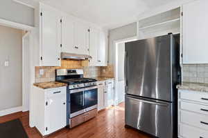 Kitchen featuring appliances with stainless steel finishes, white cabinets, dark wood-style flooring, and light stone countertops