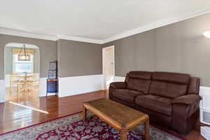 Living room featuring wainscoting, wood finished floors, a decorative wall, arched walkways, and crown molding