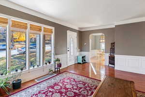 Foyer entrance featuring wood finished floors, arched walkways, a wainscoted wall, and a decorative wall