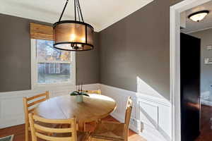 Dining space with a chandelier, wood finished floors, a wainscoted wall, ornamental molding, and a decorative wall