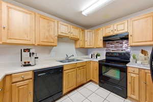 Kitchen with black appliances, light countertops, light wood finish cabinetry, decorative backsplash, and light tile patterned floors