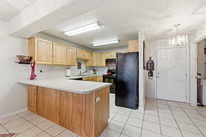 Kitchen with light countertops, a peninsula, black appliances, light tile patterned floors, and light brown cabinets