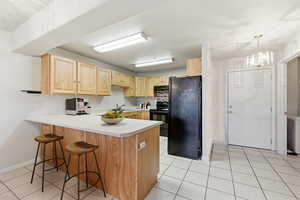 Kitchen featuring light wood finish cabinetry, black appliances, light countertops, a peninsula, and hanging lights