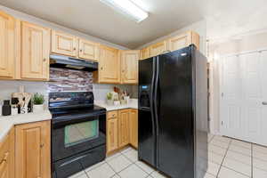 Kitchen featuring black appliances, light wood finish cabinetry, decorative backsplash, light countertops, and light tile patterned floors