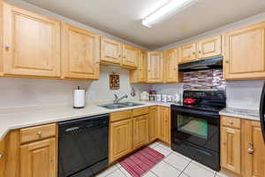 Kitchen featuring black appliances, light countertops, light tile patterned flooring, under cabinet range hood, and backsplash