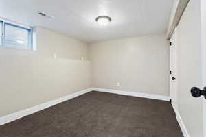 Empty room with dark carpet and a textured ceiling