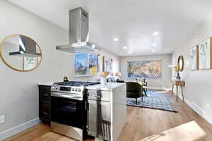 Kitchen featuring stainless steel gas range oven, light wood-type flooring, island range hood, light stone countertops, and recessed lighting