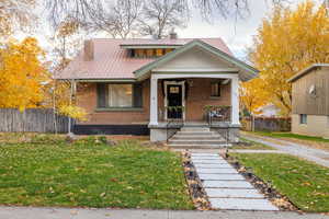 View of front facade with a porch, a metal roof, a chimney, and brick siding