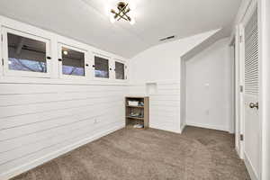 Unfurnished bedroom with a textured ceiling, lofted ceiling, carpet floors, and wood walls