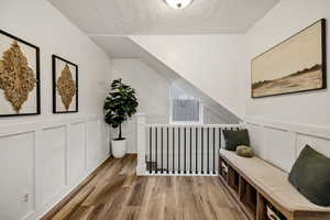 Hallway featuring a decorative wall, wood finished floors, a textured ceiling, and a wainscoted wall