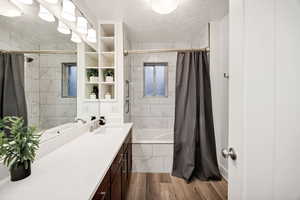 Bathroom with tiled shower / bath combo, a textured ceiling, vanity, and dark wood-type flooring