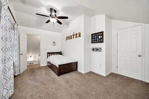 Carpeted bedroom featuring vaulted ceiling, a textured ceiling, and a ceiling fan