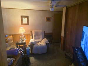 Sitting room featuring wood walls, a wainscoted wall, carpet flooring, ornamental molding, and ceiling fan