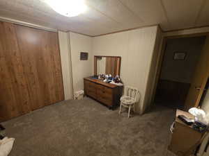 Carpeted bedroom with a closet, ornamental molding, wood walls, and a textured ceiling