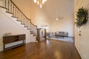 Living area with stairs, high vaulted ceiling, a decorative wall, dark wood floors, and a ceiling fan