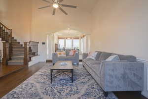 Living area featuring dark wood floors, stairs, high vaulted ceiling, arched walkways, and decorative columns